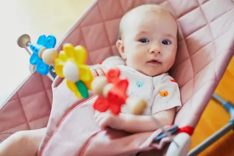 Söt bebis i en rosa babysitter vagga med färgglada leksaker.
